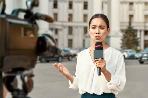 The whole truth and nothing but the truth. TV reporter presenting the news outdoors. Journalism industry, live streaming concept. Cropped portrait of professional female reporter at work. Young woman standing on the street with a microphone in hand and smiling at camera. Horizontal shot. Selective focus on woman blouse photos stock pictures, royalty-free photos & images