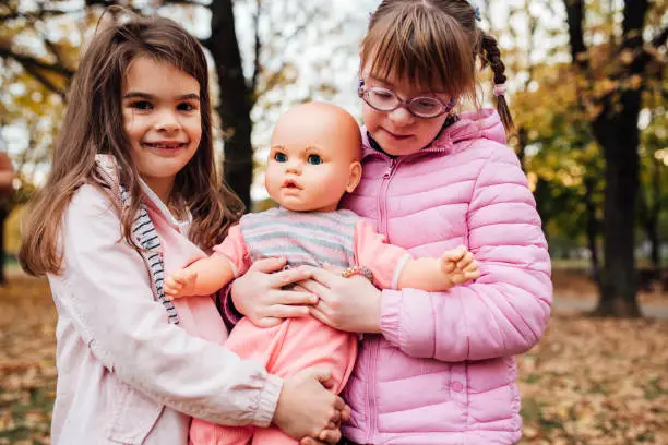 Photo of Cute girl with Down syndrome playing with her friend in the park