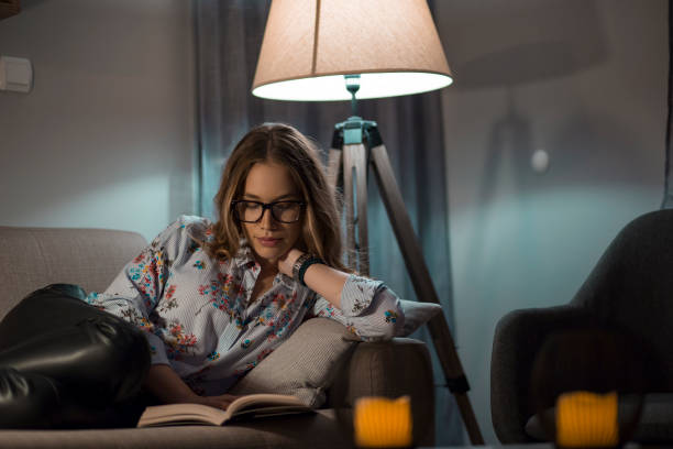 istock Young female reading book in living room 1187648413