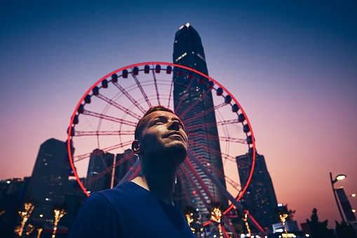 Nightlife in Hong Kong. Young man (traveler) against ferris wheel and urban skyline.