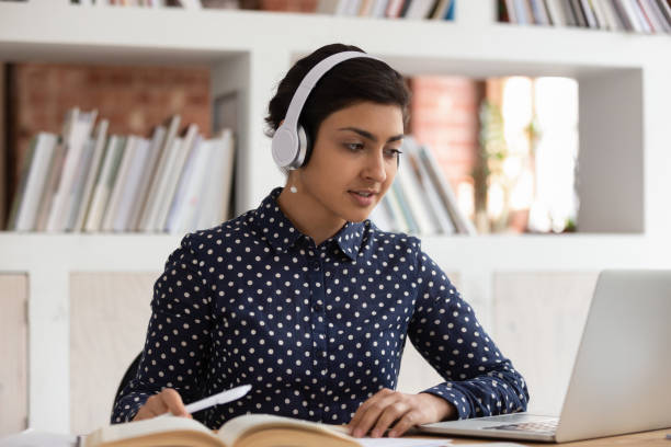 istock Indian girl in headphones do assignment in library using computer 1187656872