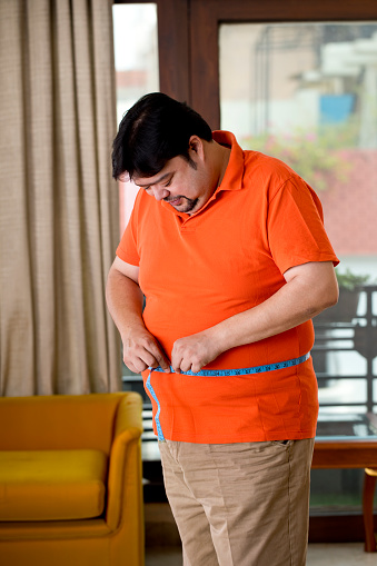 Overweight man measuring his waist size with tape measure