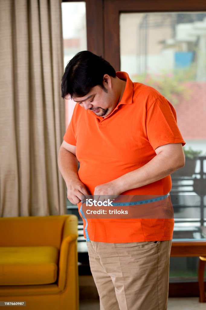 Obese man measuring his belly Overweight man measuring his waist size with tape measure Dieting Stock Photo