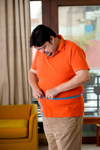 Obese man measuring his belly Overweight man measuring his waist size with tape measure body conscious stock pictures, royalty-free photos & images