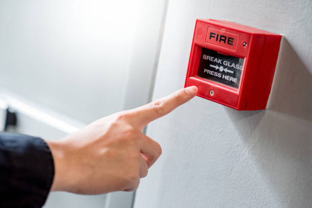 Male hand pointing at red fire alarm switch Male hand pointing at red fire alarm switch on concrete wall in office building. Industrial fire warning system equipment for emergency. emergency break glass box stock pictures, royalty-free photos & images