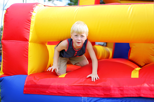 A cute little kid is playing on an inflatable bounce house obstacle course at a Small town American festival.