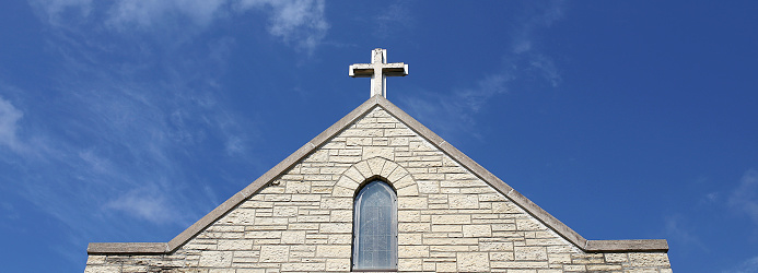 A small cross sits atop a temple steeple on an old stone Christian Church.