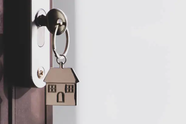The home key with house keyring in the door keyhole with copy space. The concept of renting or selling a house or flat, mortgage and real estate, property buying.