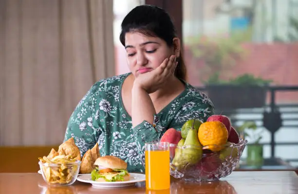 Displeased woman thinking what to eat between healthy and unhealthy food on table