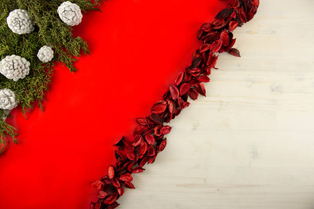 istock Flat lay red Christmas copy space with a diagonal red stripe on light wooden background, pine branches, white pine cones and red petals 1187666672