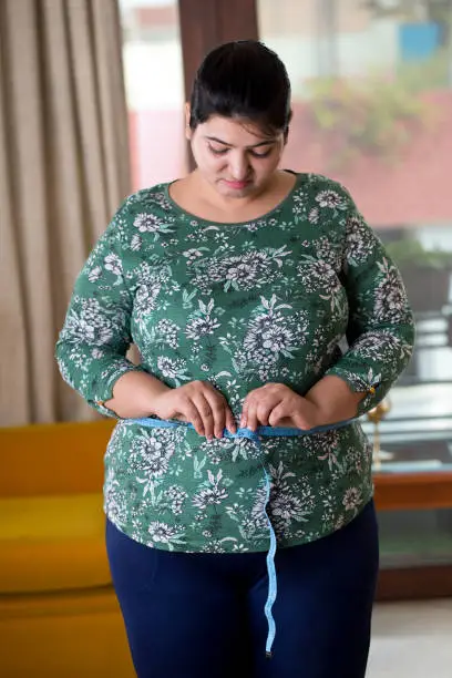 Overweight woman measuring her waist size with tape measure