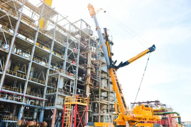 Construction and installation work with a powerful construction crane of a large new industrial oil refining petrochemical chemical plant with pipes, columns, railings, stairs and equipment.