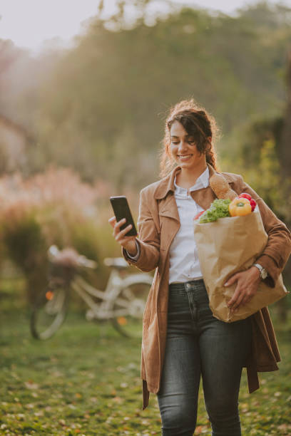 istock Woman using smart phone and holding groceries bag 1187672575