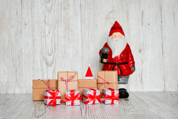 istock Selective focus santa claus statue with set of gift boxes tight with red ribbins, handmade objects on wood gray background. Christmas holiday concept. 1187674925