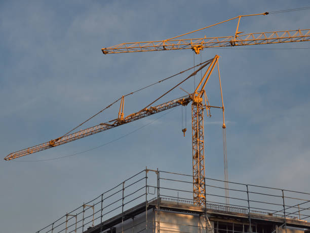 istock Two construction tower cranes over a building under construction with workers in silhouette 1187679087