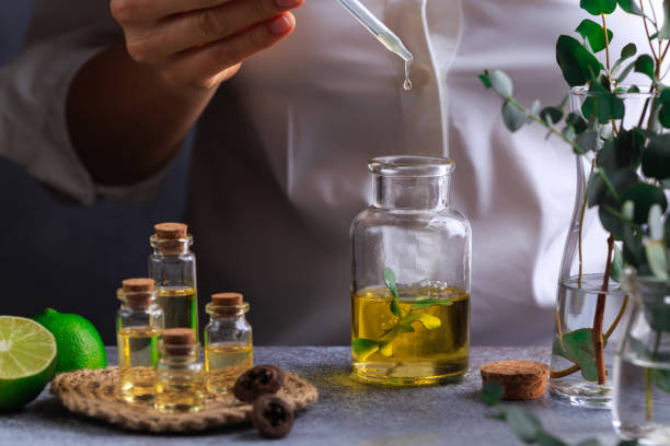 Woman hand pouring eucalyptus essential oil into bottle on grey table stock photo