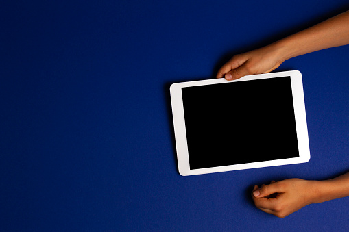 Kid hands holding white tablet computer on navy blue background.