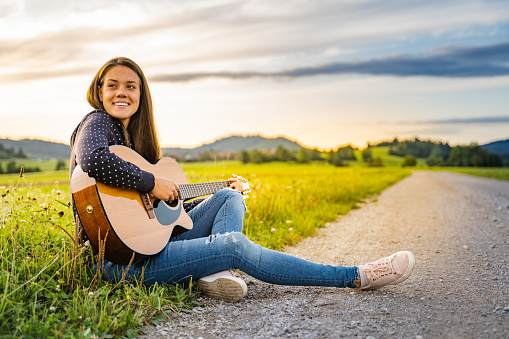 Fashionable woman playing acoustic guitar on a side of a country road - stock photo