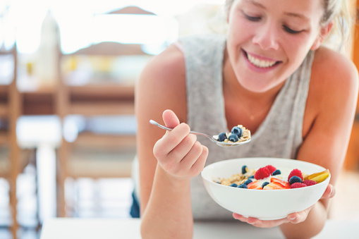 Happy woman Eating healthy breakfast bowl. It includes strawberries, blueberries, kiwifruit, granola, muesli  and yoghurt. Clean eating, dieting, detox, vegetarian food concept.