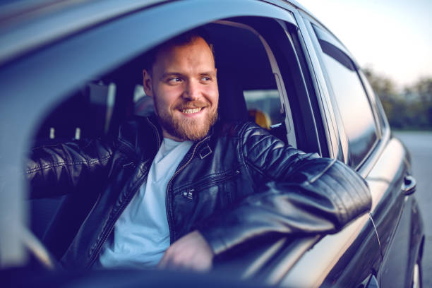 istock Young handsome smiling bearded blond caucasian man in leather jacket posing in his modern car. 1187698416