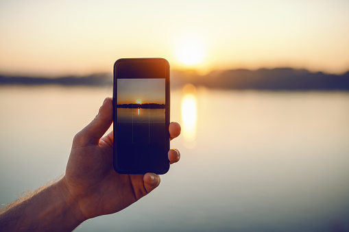 Close up of Caucasian man taking picture with smart phone of beautiful sunset.