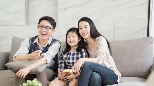 happy asian family watching tv together on sofa in living room. family and home concept happy asian family watching tv together on sofa in living room. family and home concept asian kids watching tv stock pictures, royalty-free photos & images