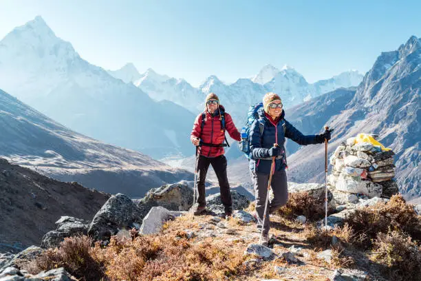 Photo of Couple following Everest Base Camp trekking route near Dughla 4620m. Backpackers carrying Backpacks and using trekking poles and enjoying valley view with Ama Dablam 6812m peak