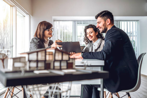 Side view image of young happy family sitting in consulting office, making property purchase. Mature female Real Estate Agent helping business couple do financial investment. Installment payment, mortgage, loan for estate concept Side view image of young happy family sitting in consulting office, making property purchase. Mature female Real Estate Agent helping business couple do financial investment. Installment payment, mortgage, loan for estate concept real estate office stock pictures, royalty-free photos & images