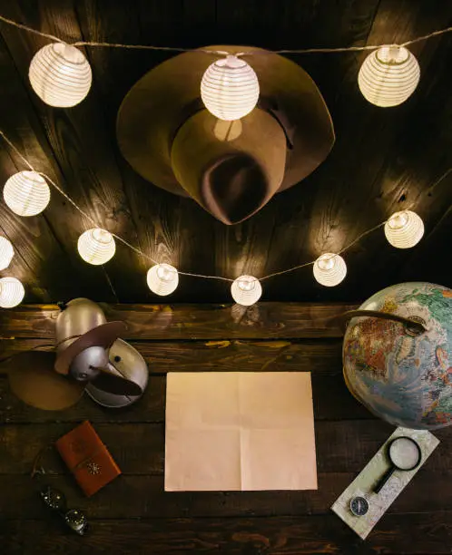Overhead night view of traveler's desk while writing a letter, making a plan of a trip in remote, off grid wooden hut. Empty space for copy, room for text. Analog wild holiday vibe wanderlust concept. Dark vertical shot.