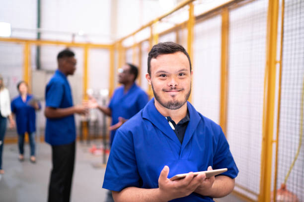 Portrait of special needs employee holding digital tablet in industry Portrait of special needs employee holding digital tablet in industry down syndrome photos stock pictures, royalty-free photos & images