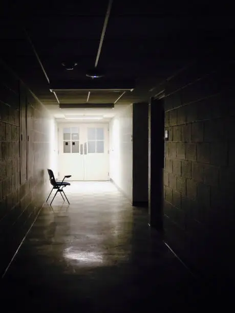 An Empty School Chair Leaning Against a Wall in a Dark, Forboding Classroom Hallway