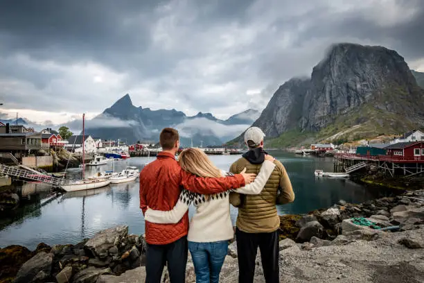 Homosexual couple with their sister-in-law visiting the fishing village of Hamnøy in the Lofoten Islands with mountain range and cloudy sky in background during summer.