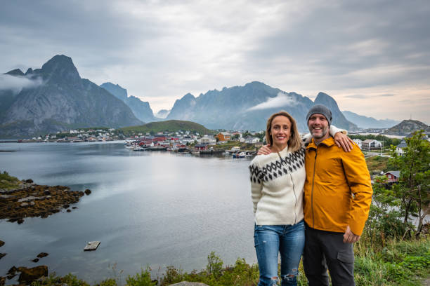Couple visiting a fishing village. Couple visiting the fishing village of Reine in the Lofoten Islands with mountain range and cloudy sky in background during summer. reine lofoten stock pictures, royalty-free photos & images