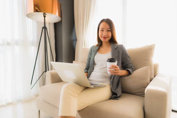 istock Beautiful young asian portrait using computer and laptop with coffee cup sitting on sofa 1187733901