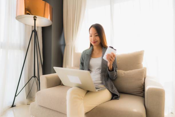 istock Beautiful young asian portrait using computer and laptop with coffee cup sitting on sofa 1187734084