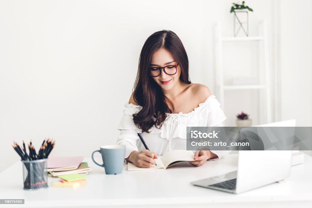 Girl student sitting and studying and learning online with laptop computer and reading a book before the exam at home.education concept Adult Stock Photo