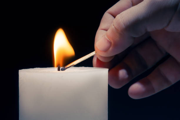 istock Man lights a festive white candle, on a dark background 1187746311