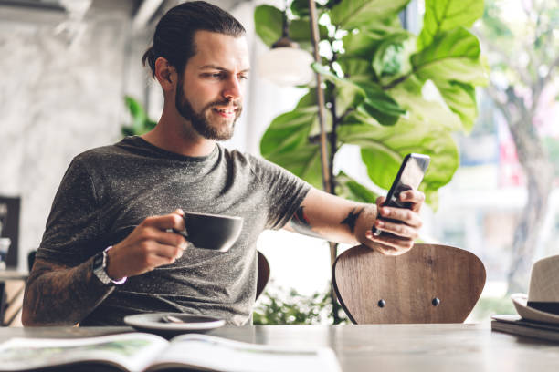 istock Handsome bearded hipster man use smartphone with coffee at table in cafe.Communication and technology concept 1187746647