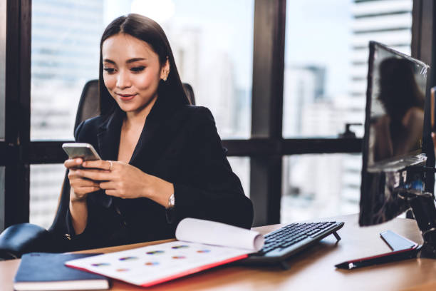 istock Businesswoman in elegant black suit working and use smartphone with computer sitting at table in office 1187746699