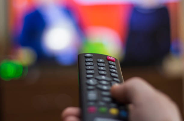 istock Hand holding TV remote control with TV in background 1187769508