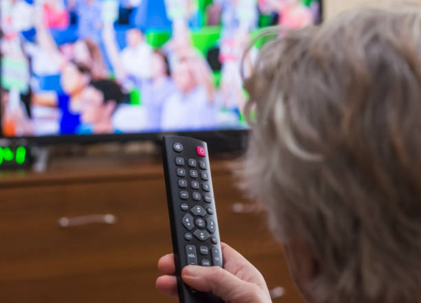 istock Rear view a gray-haired middle-aged woman controls the TV with a remote control 1187769512