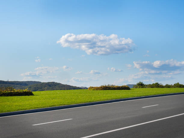 istock Autumn landscape with asphalt road, green lawn under sky with clouds 1187777452