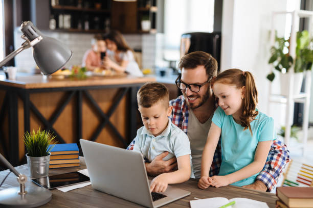 istock Father with daughter and son on his lap using laptop at home 1187794683