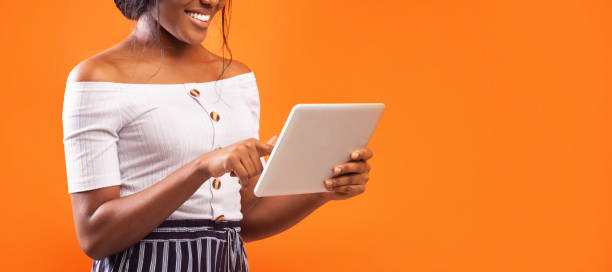 istock Unrecognizable Afro Girl Using Tablet Over Orange Background, Cropped, Panorama 1187795877