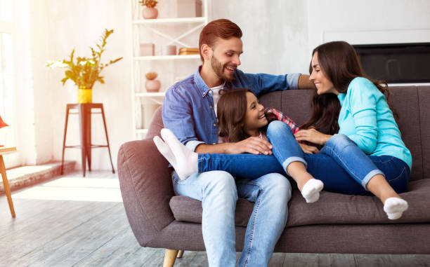 Happy childhood. A beautiful family of father, daughter and mom are sitting on the sofa at home, laughing, hugging and playing with each other. shielding photos stock pictures, royalty-free photos & images