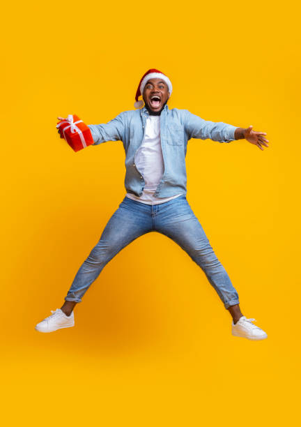 istock Overjoyed afro guy in santa hat jumping with gift box 1187798091