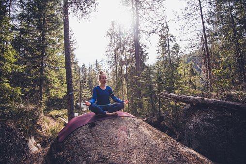 Young female doing yoga in evergreen forest.