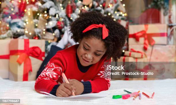 Little Black Girl Lying On Floor Writing Letter To Santa - Fotografias de stock e mais imagens de Carta - Documento
