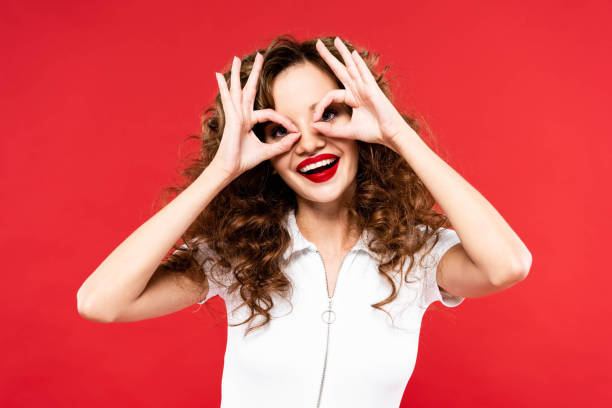istock funny curly girl making eyeglasses from hands, isolated on red 1187799328