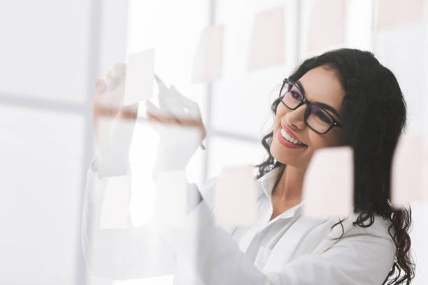 istock Mexican woman writing ideas on sticky notes over glass wall 1187799832
